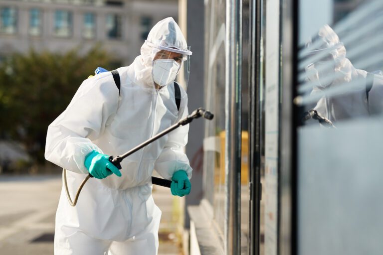Disinfection worker in protective suit spraying public buildings in order to prevent the spread of COVID-19.